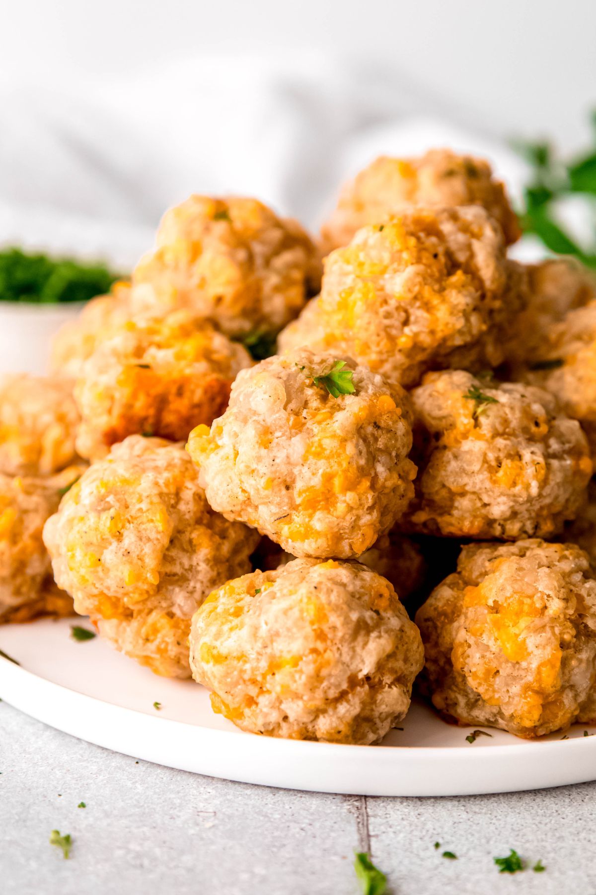 pile of bisquick-free sausage balls on a white plate with a sparse sprinkling of fresh parsley.