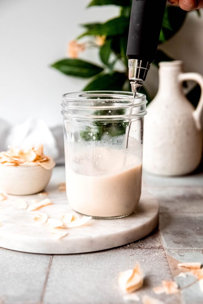 action shot of a milk frother whisking together the milk and protein powder in a mason jar.