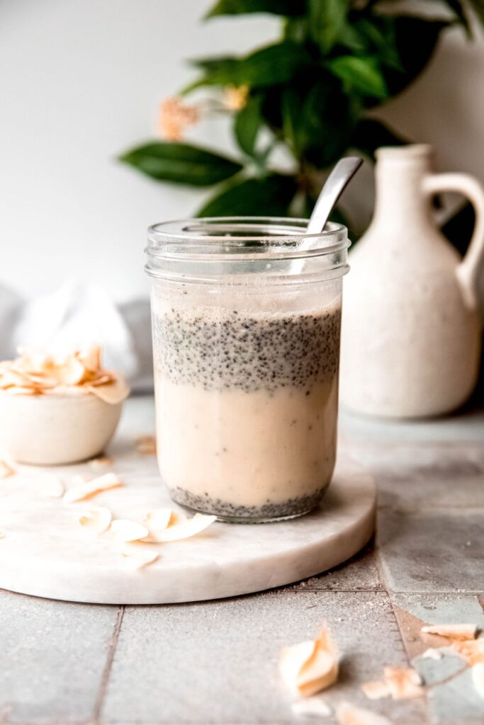 silver spoon in a jar of coconut chia pudding after the chia seeds have floated to the top; it's time to stir it again before putting in the fridge overnight.