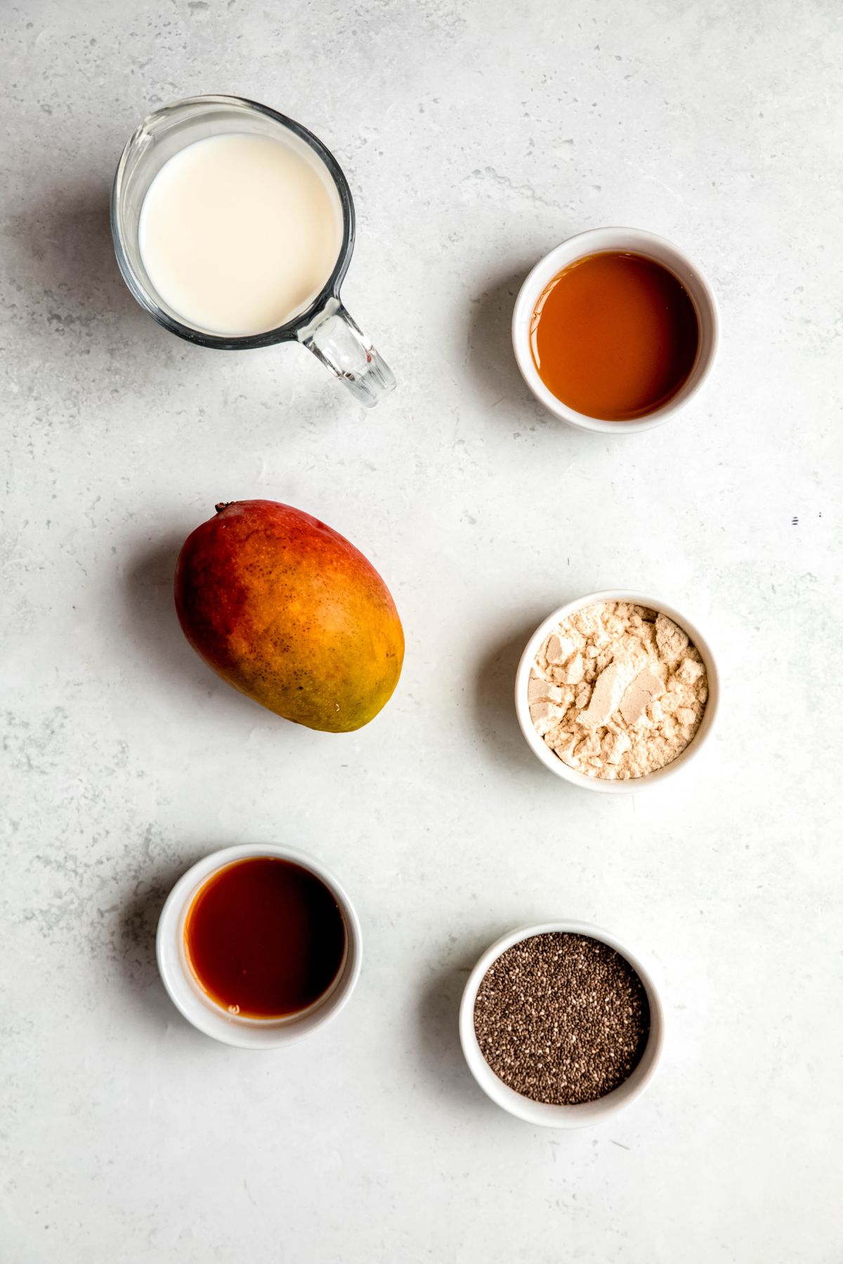 ingredients for making coconut mango chia seed pudding with protein powder measured out on a white table.