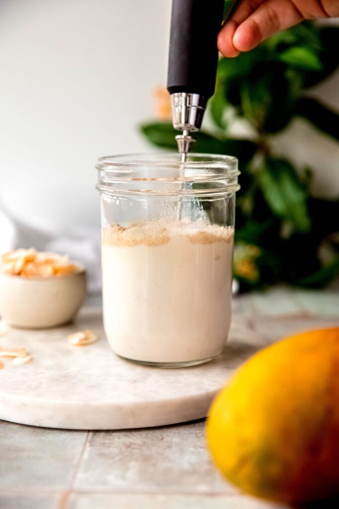 action shot of a hand holding a milk frother that is whisking the milk and protein powder together in a mason jar.