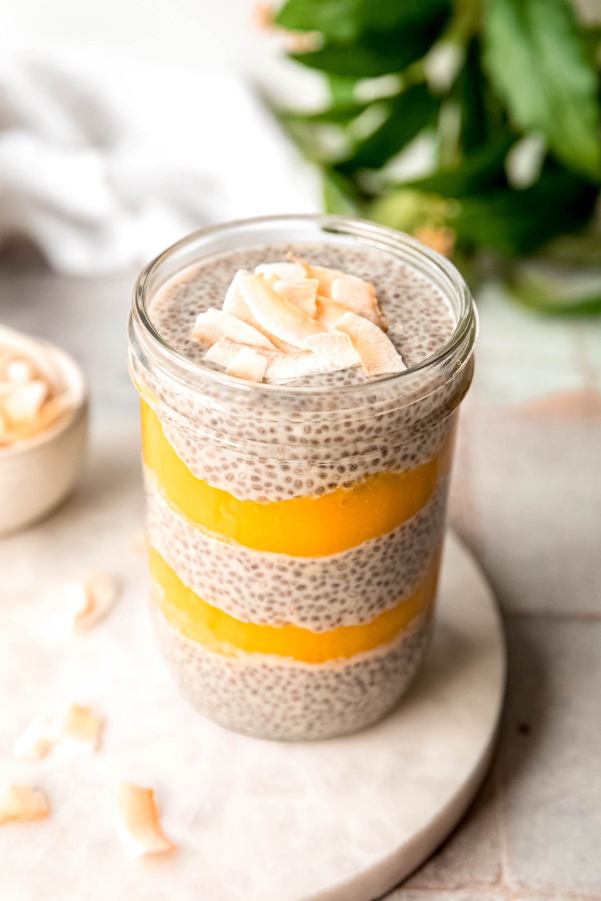 45 degree angle shot of high protein mango chia seed pudding in a mason jar topped with coconut flakes.