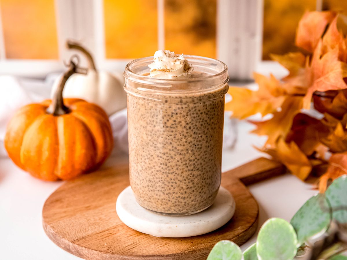 horizontally framed hero shot of a mason jar of chia seed pumpkin pudding on a table with fall decor like miniature pumpkins and a bunch of fall leaves.