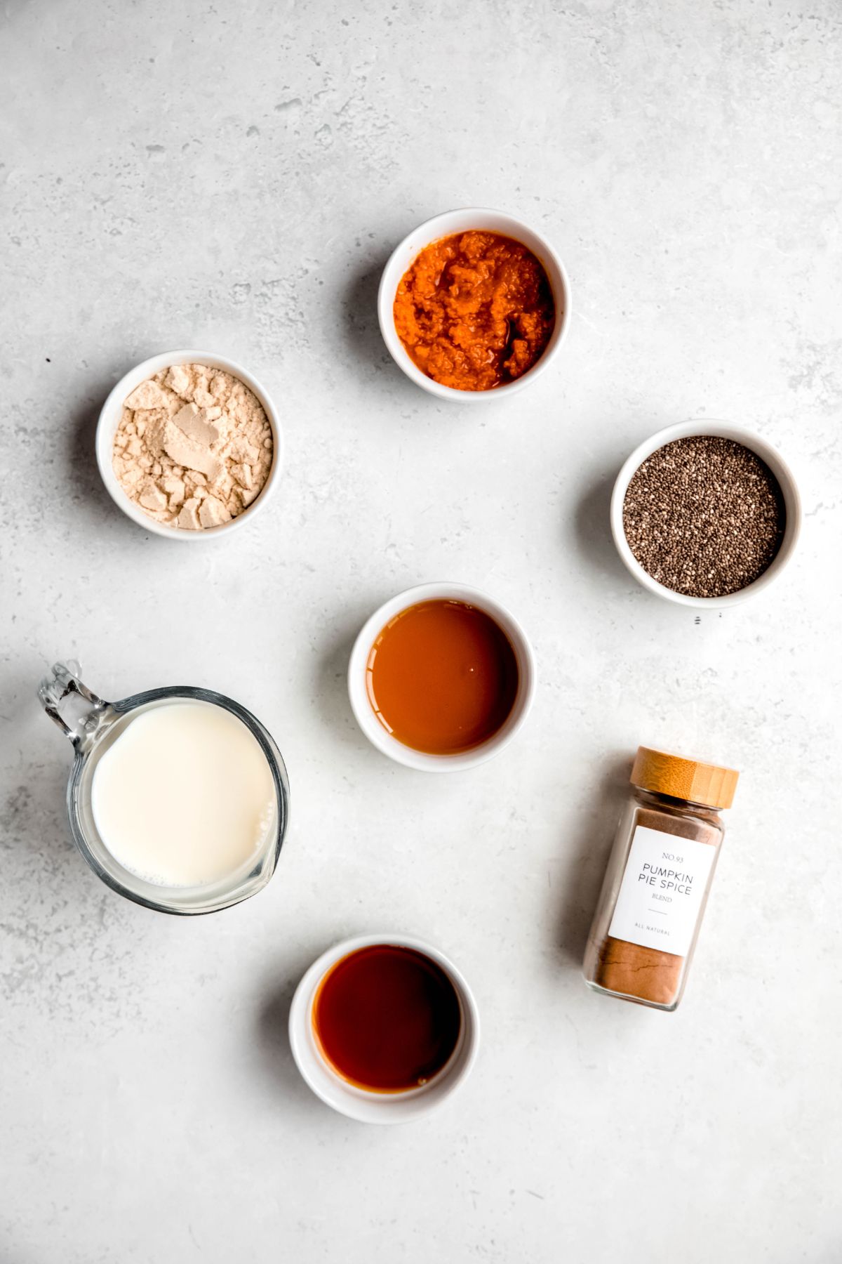 flat lay shot of the ingredients needed to make high protein pumpkin chia seed pudding measured out on a white table.