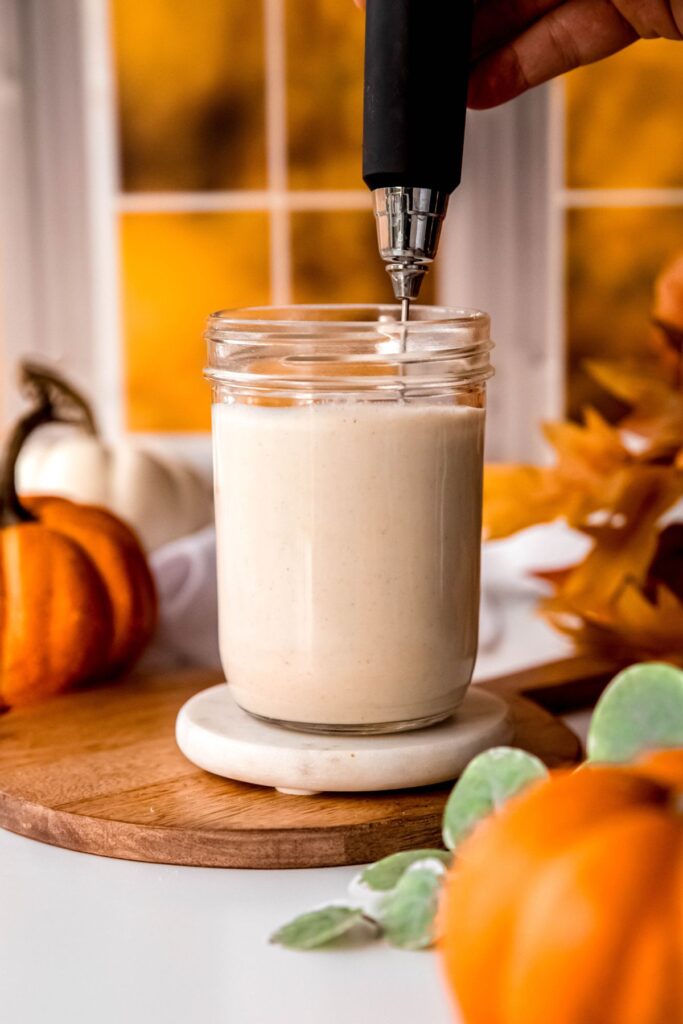 action shot of a hand using a milk frother to blend the milk and protein powder.