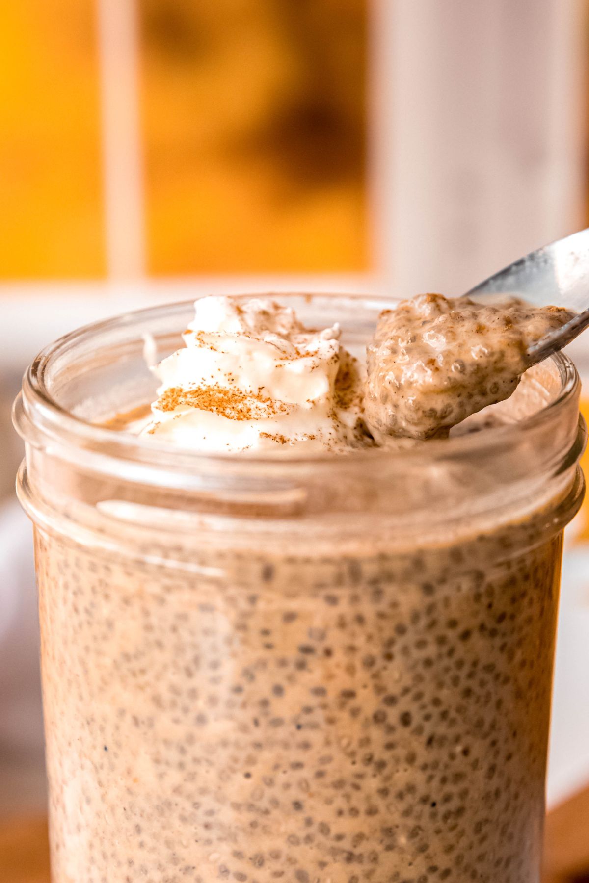 closeup shot of a silver spoon taking a bite from the jar of pumpkin chia pudding to show the thick texture.