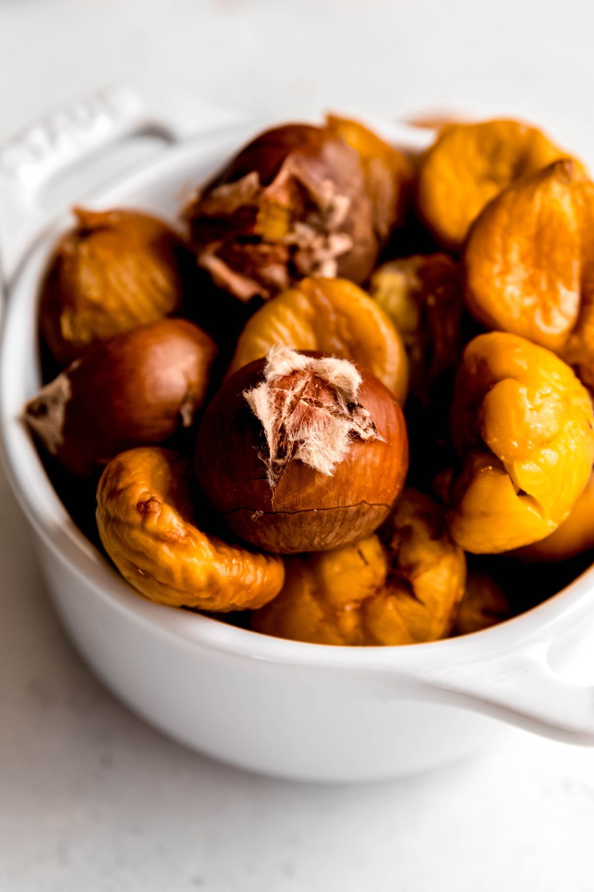 closeup shot of a bowl with half peeled and half still in their shell roasted chestnuts.