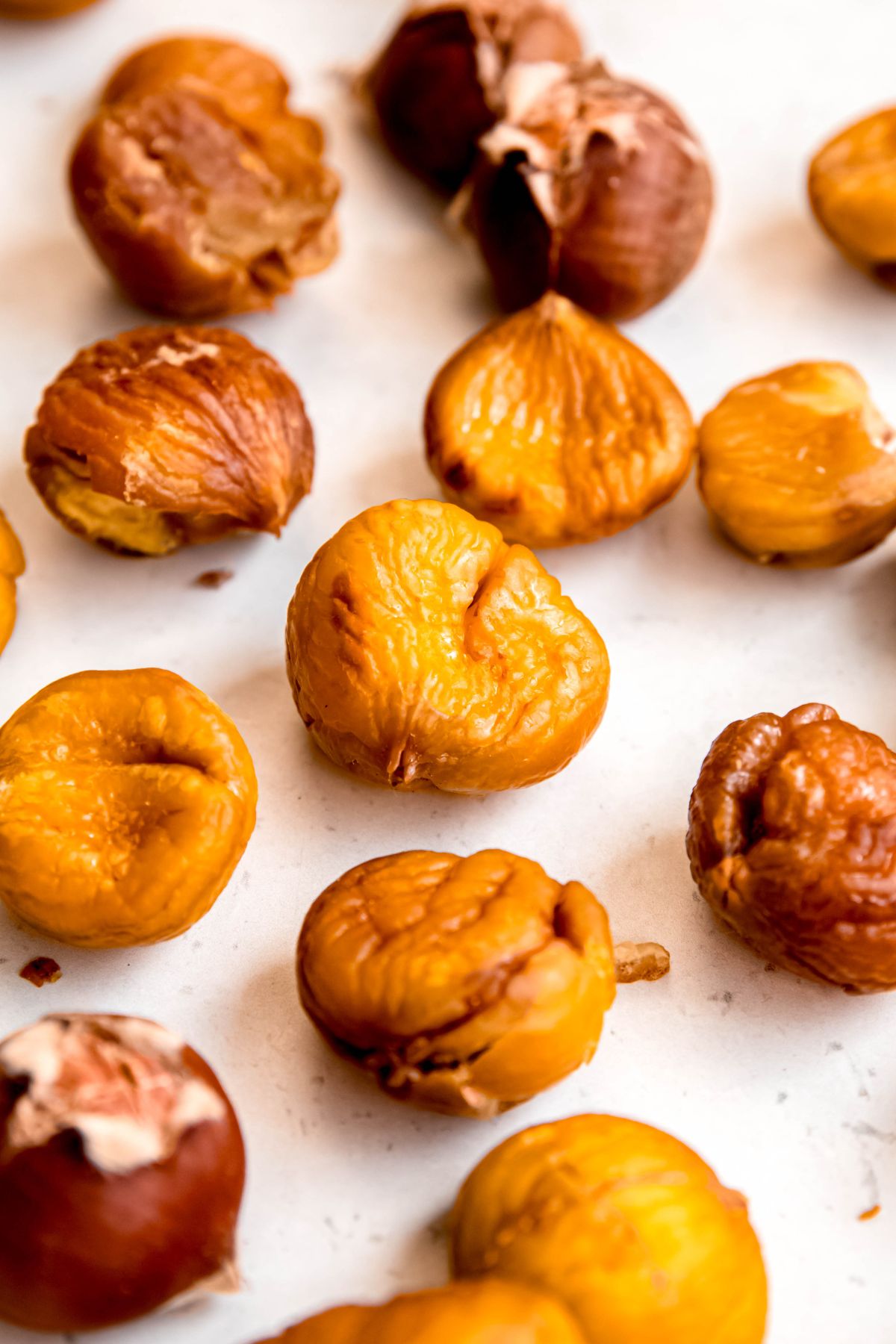 closeup shot of peeled roasted chestnuts on a white table with one still in its shell.