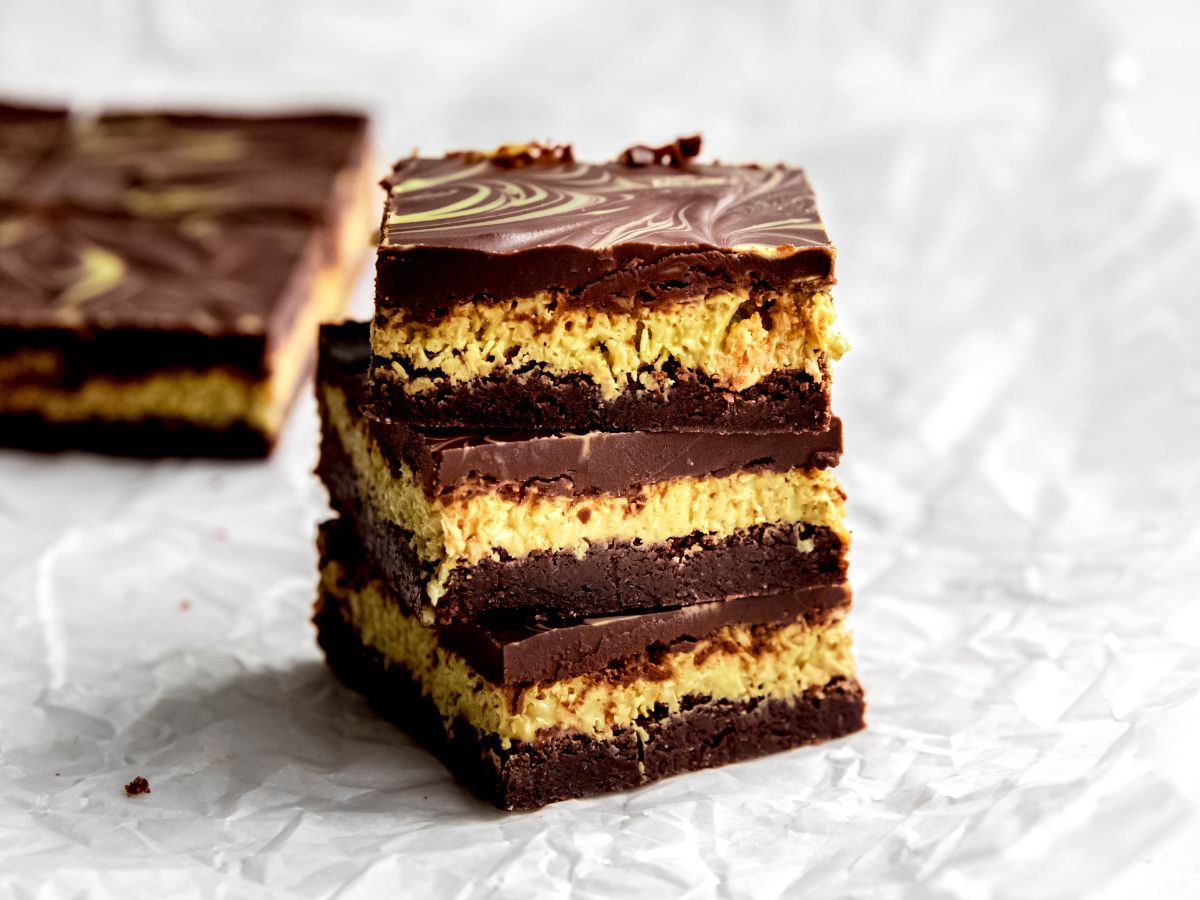 horizontally framed hero shot of a side on view of 3 dubai chocolate brownies stacked showing the distinct brownies, pistachio cream layer, and fudgy chocolate ganache layer.