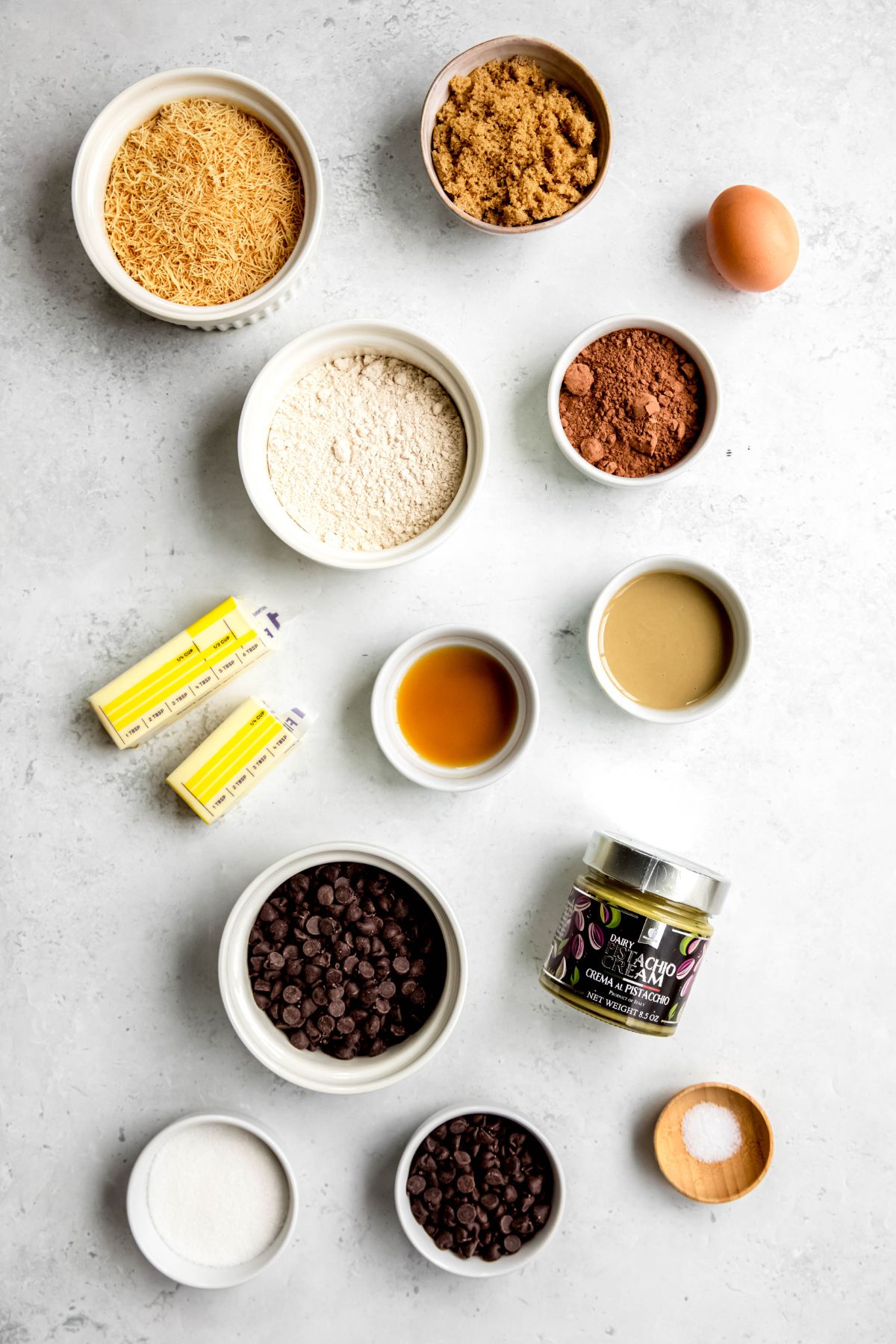 overhead shot of ingredients needed to make pistachio chocolate dubai chocolate brownies recipe measured out in white bowls on a white table.