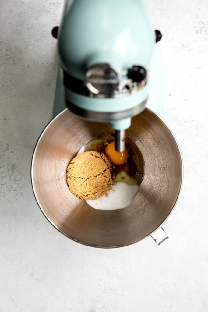 egg and sugars added to a silver mixing bowl on a stand mixer.