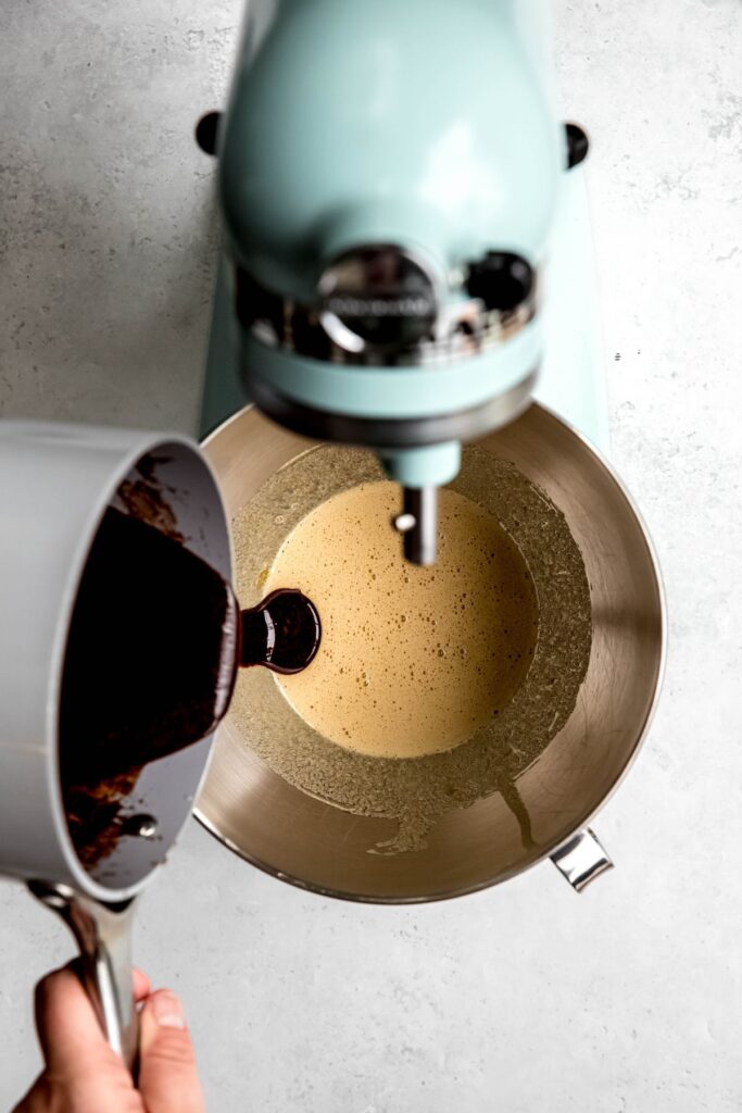 melted chocolate mixture being poured into the mixing bowl with the egg and sugar mixture.