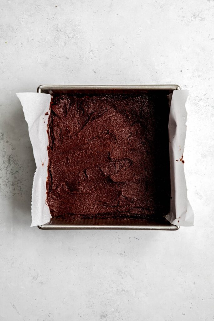 chocolate brownie batter spread out in a parchment lined pan.