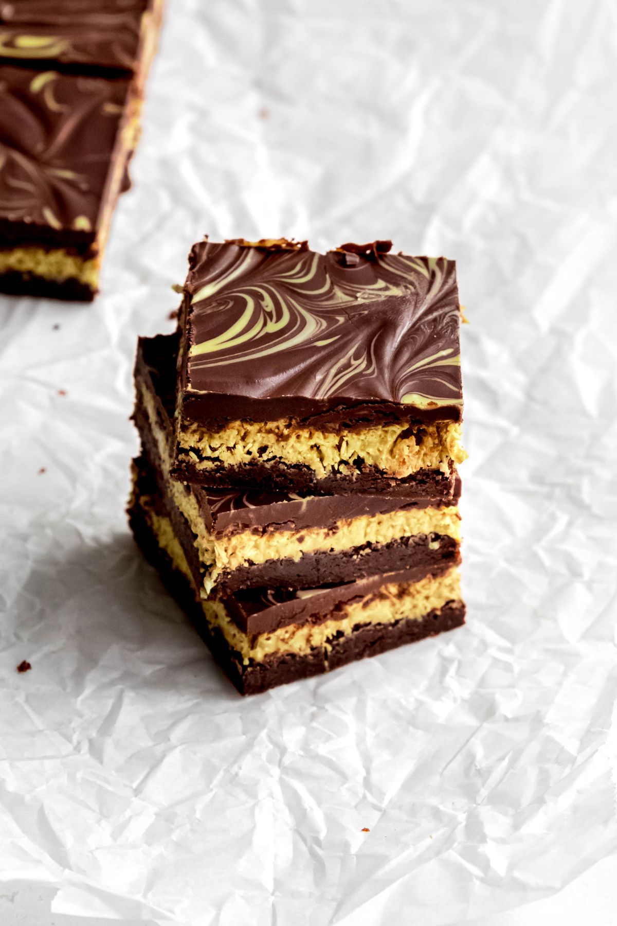 3 pistachio Dubai chocolate brownies stacked on each other on a piece of crumpled white parchment paper.