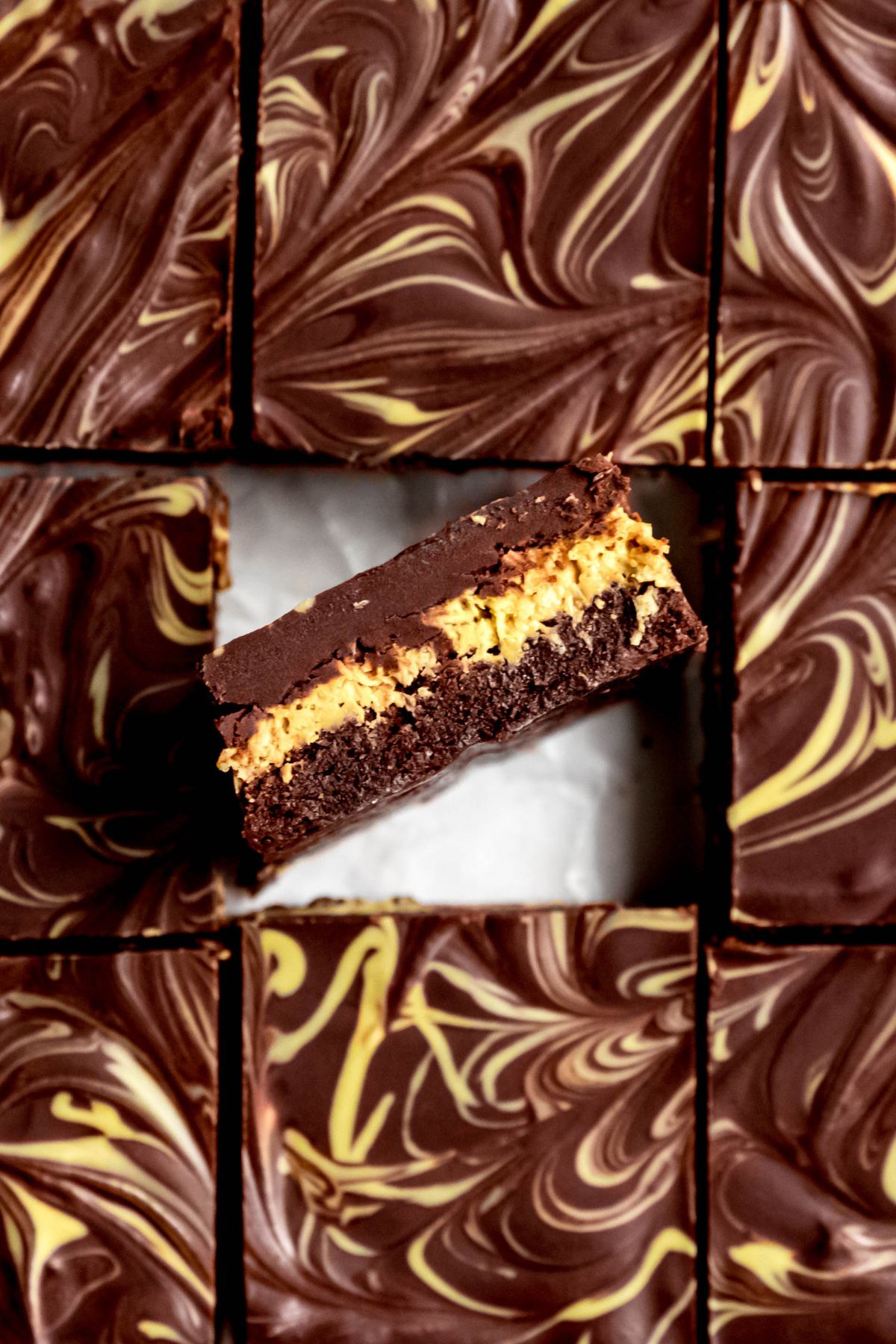 overhead closeup shot of a tray of dubai chocolate brownies with the one in the middle turned on its side so you can see the distinct layers of ganache, pistachio cream filling and chewy brownie.