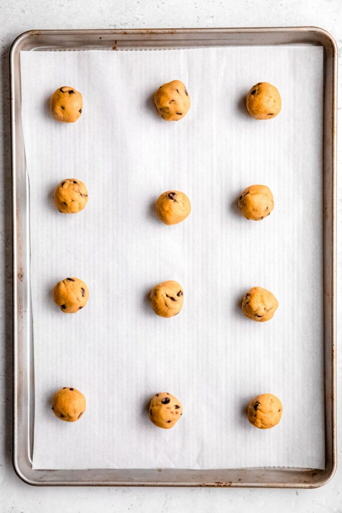 12 balls of chocolate chip cookie dough on a parchment-lined baking sheet.