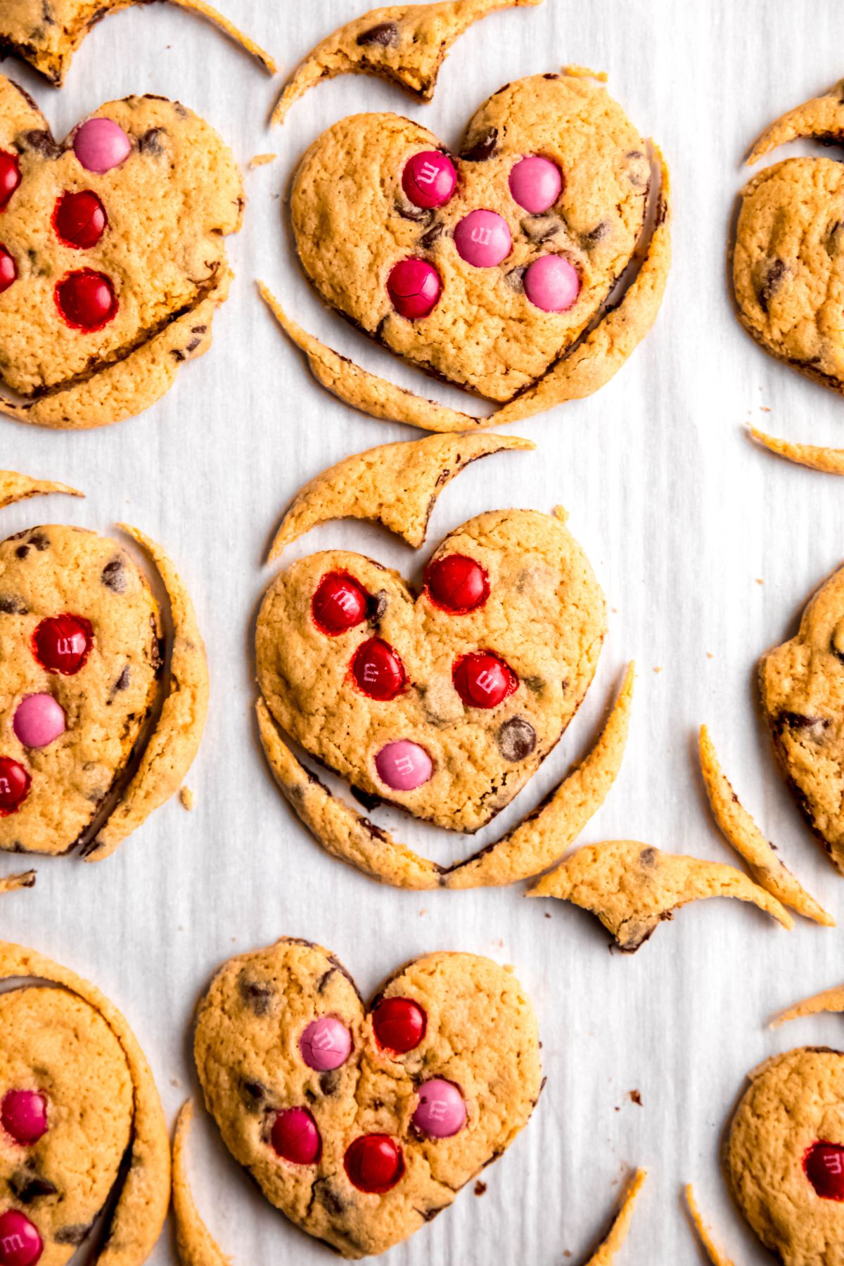 closeup shot of a tray of heart-shaped chocolate chip cookies with the scrap pieces still on the tray.
