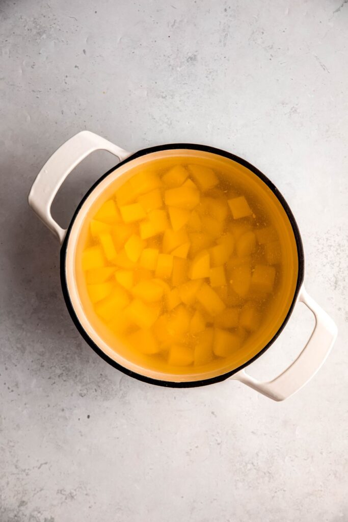 Cubes potatoes in a white pot with water.