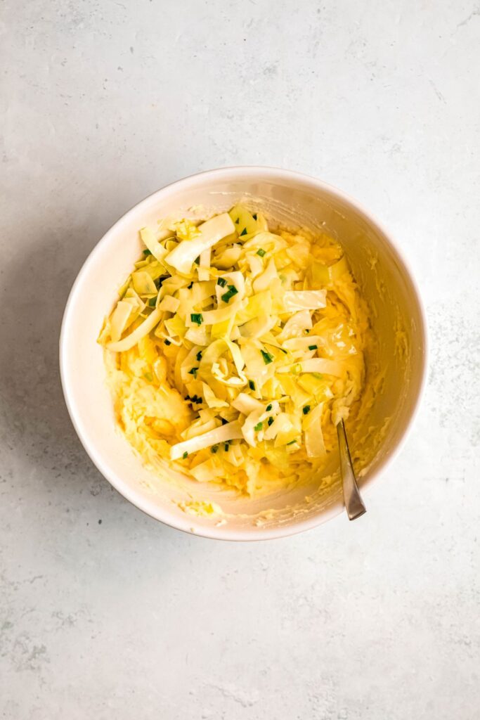 Adding the sauteed cabbage to the bowl of mashed potatoes.