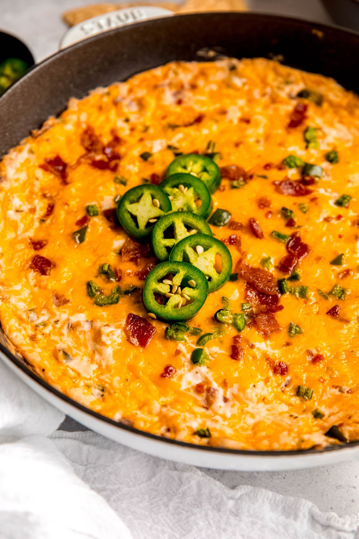 closeup shot of bacon jalapeno popper dip topped with fresh slices of jalapeños and bacon bits.