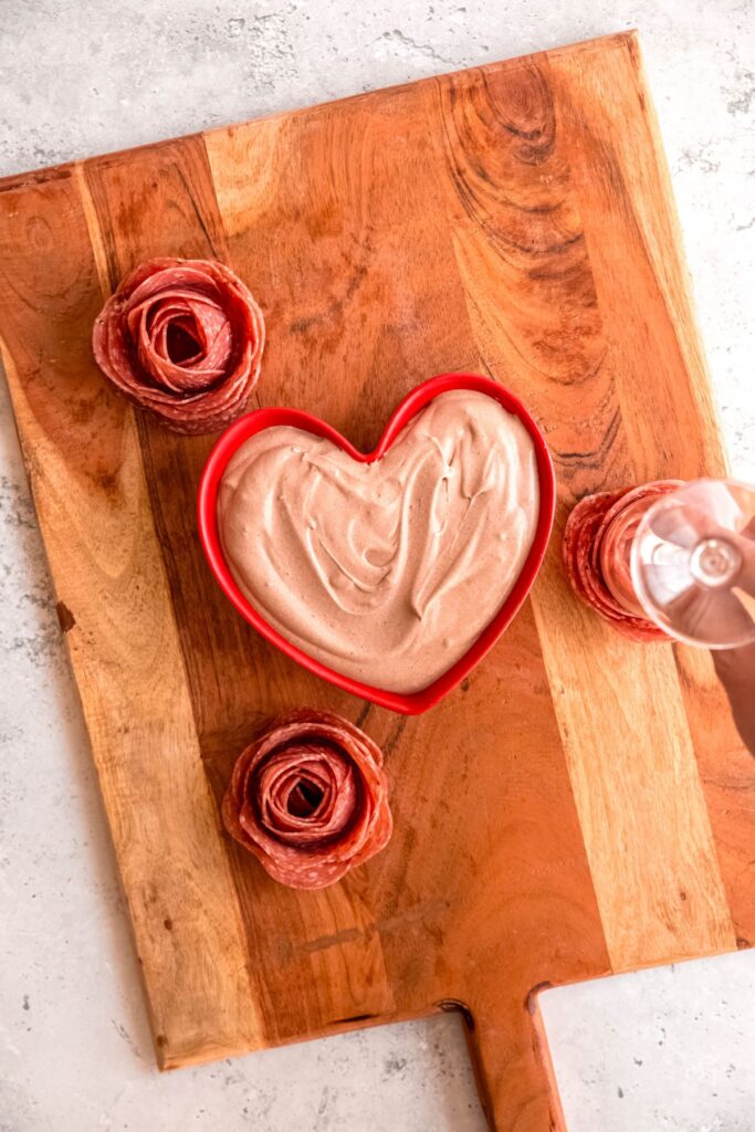 The bowl of chocolate dip and salami roses on the cutting board.