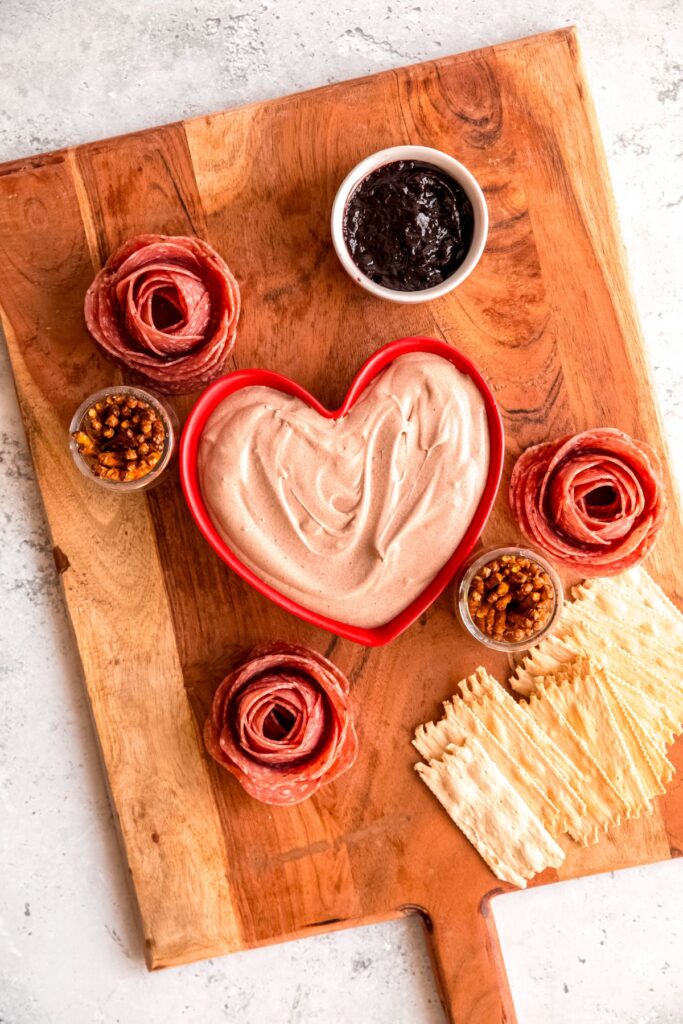 Adding the cups of pretzels, fruit preserves dip, and crackers to the cutting board.