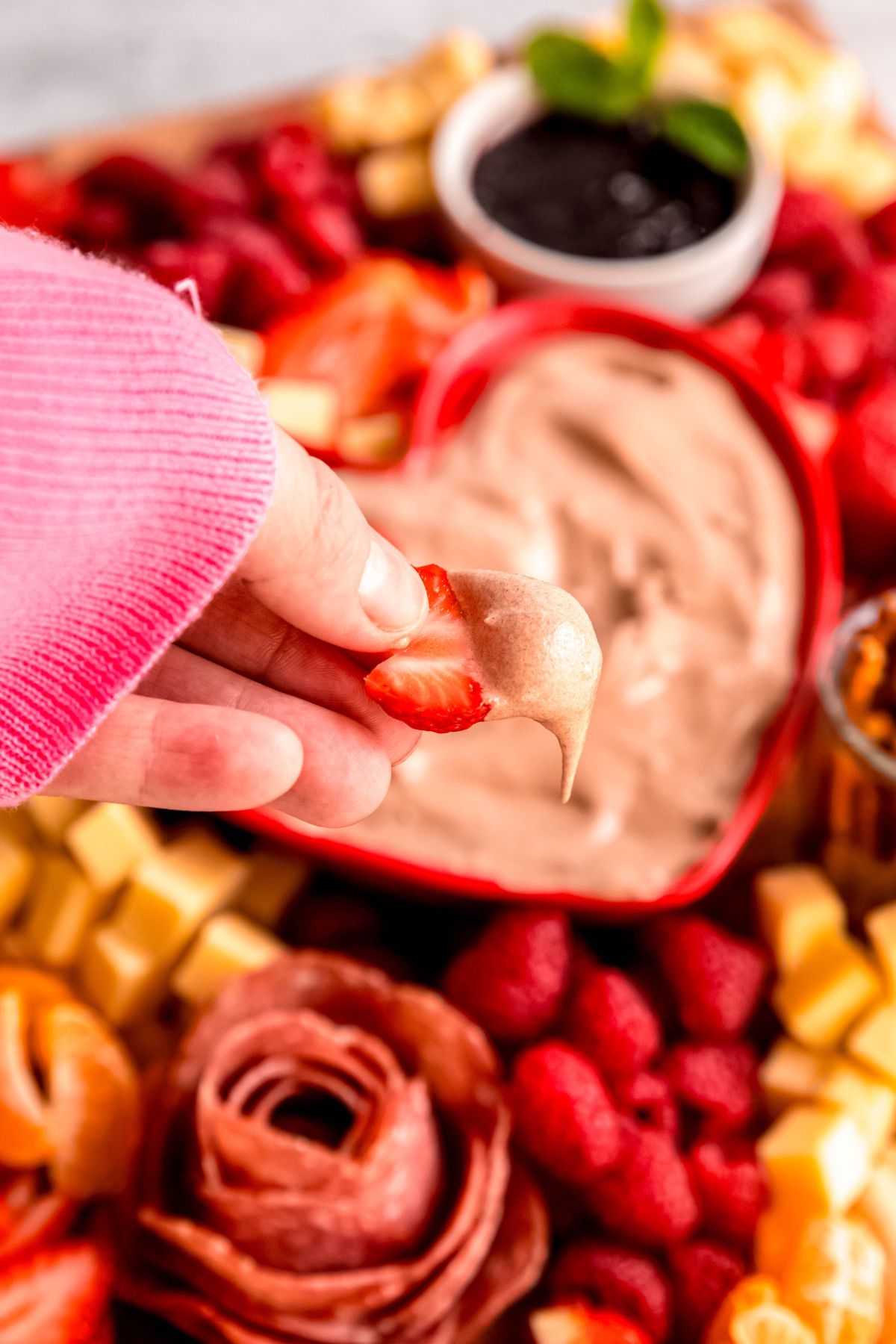 A close-up shot of a hand holding a strawberry half that's dipped in the chocolate fruit dip.