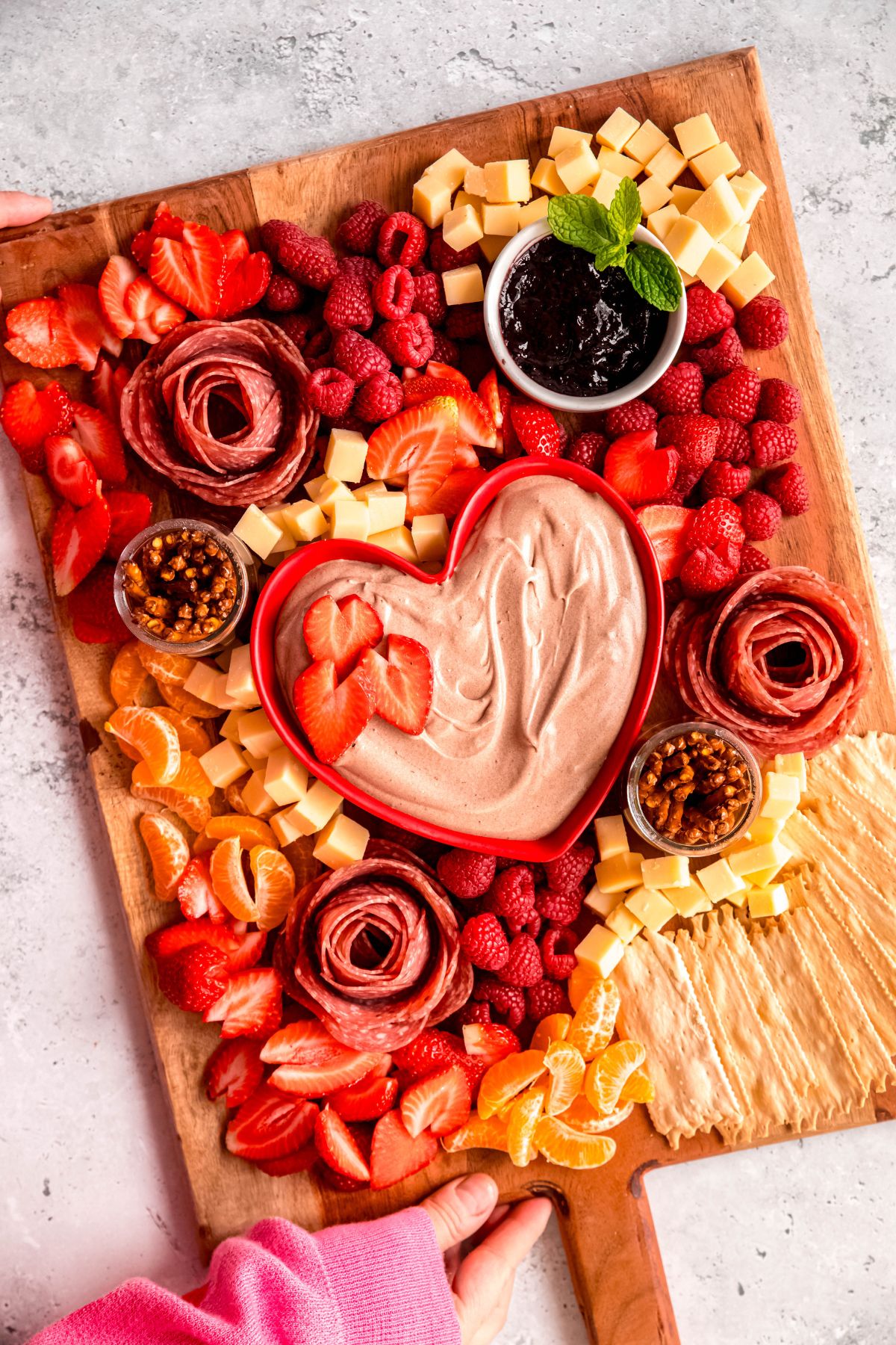 Two hands grabbing the charcuterie board to serve.