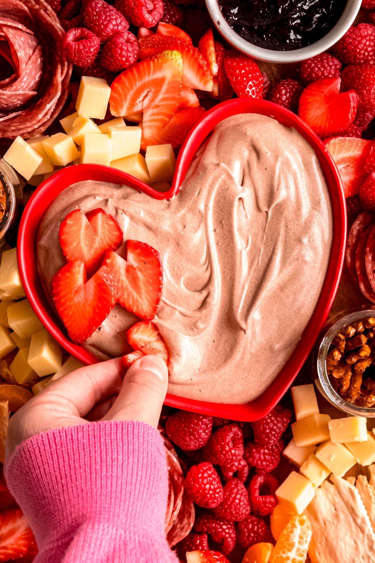 A close-up shot of a hand dipping a strawberry into the chocolate dip on the charcuterie board.