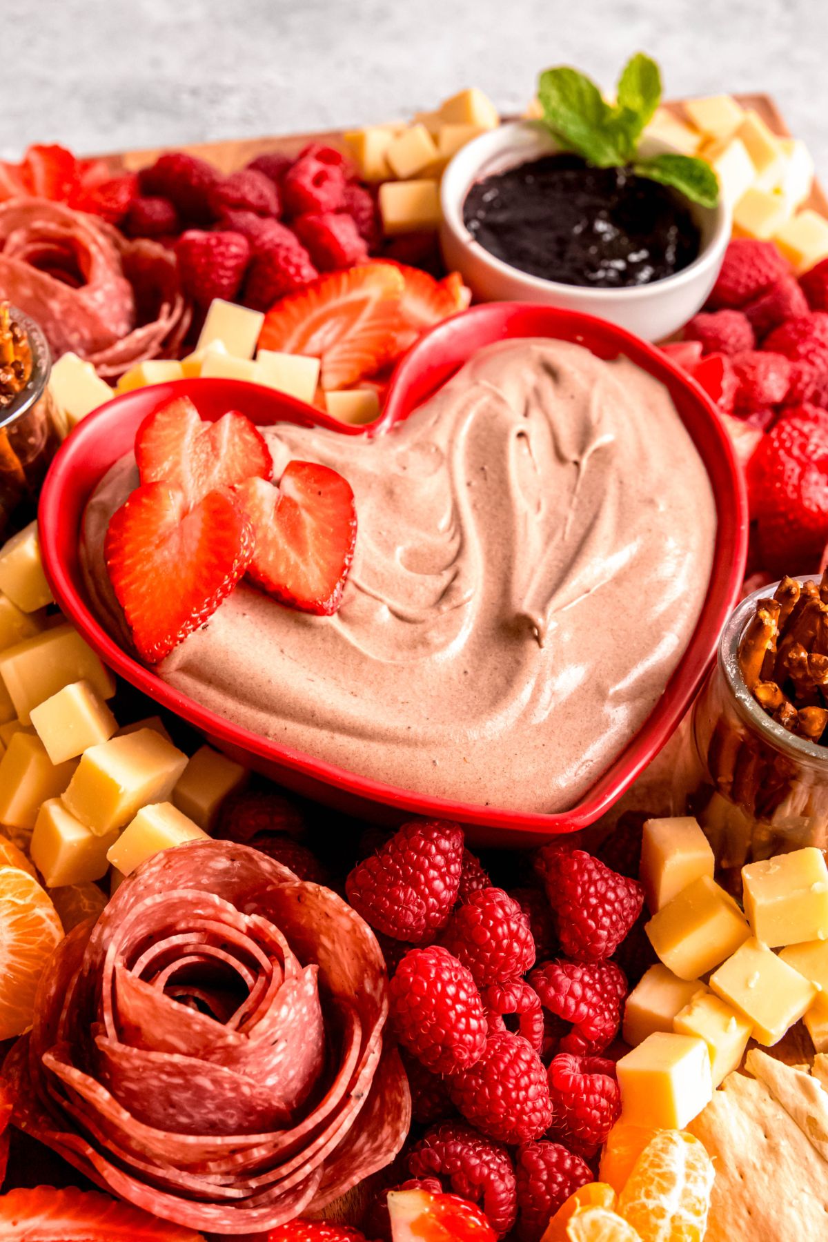 An angled close-up shot of a Valentine's Day charcuterie board with chocolate fruit dip in the center.