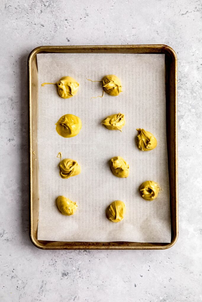 dollops of pistachio cream on a parchment paper lined baking sheet for freezing.