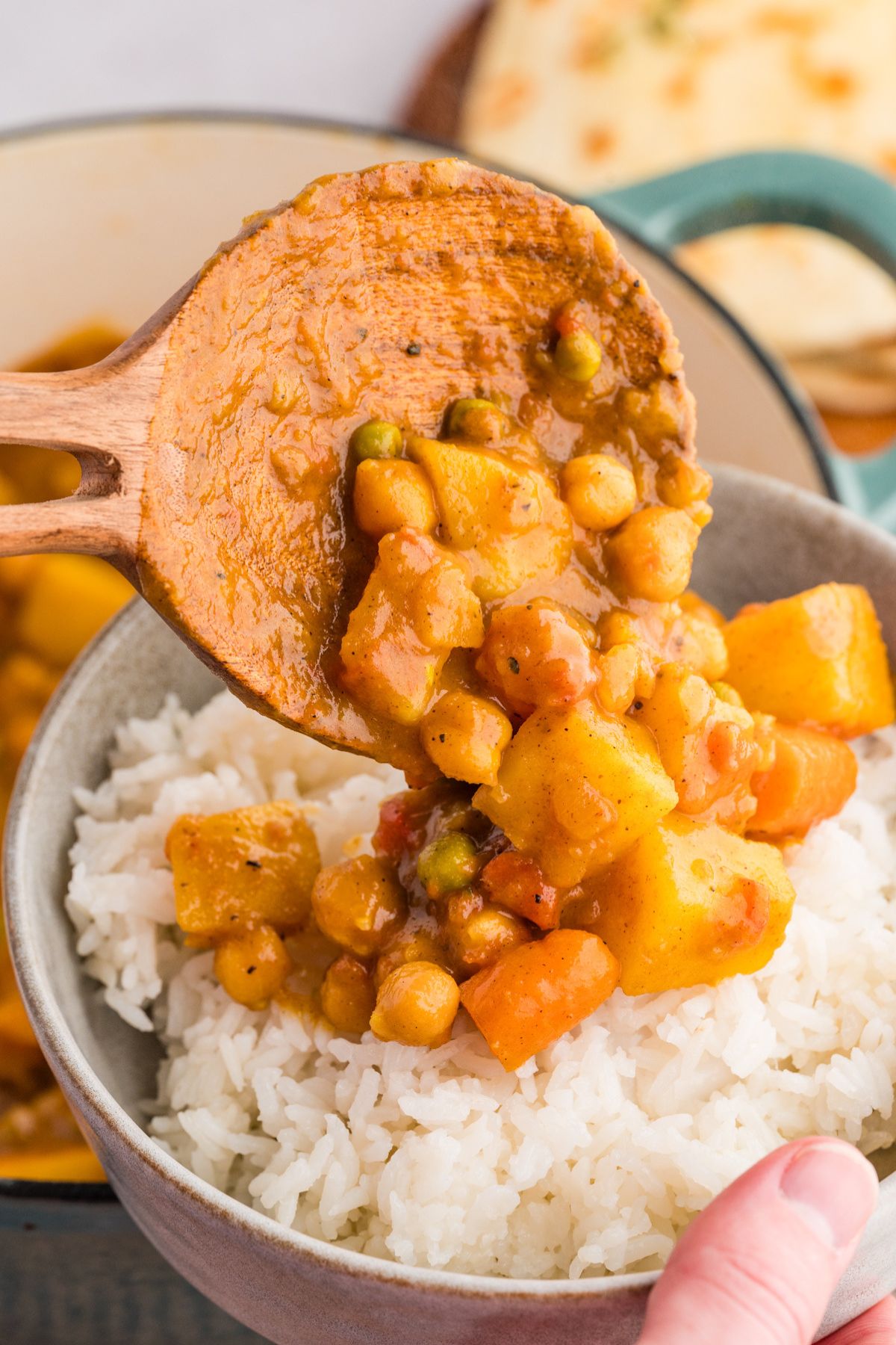 wooden serving spoon dishing out chickpea potato curry onto a bowl of white rice.