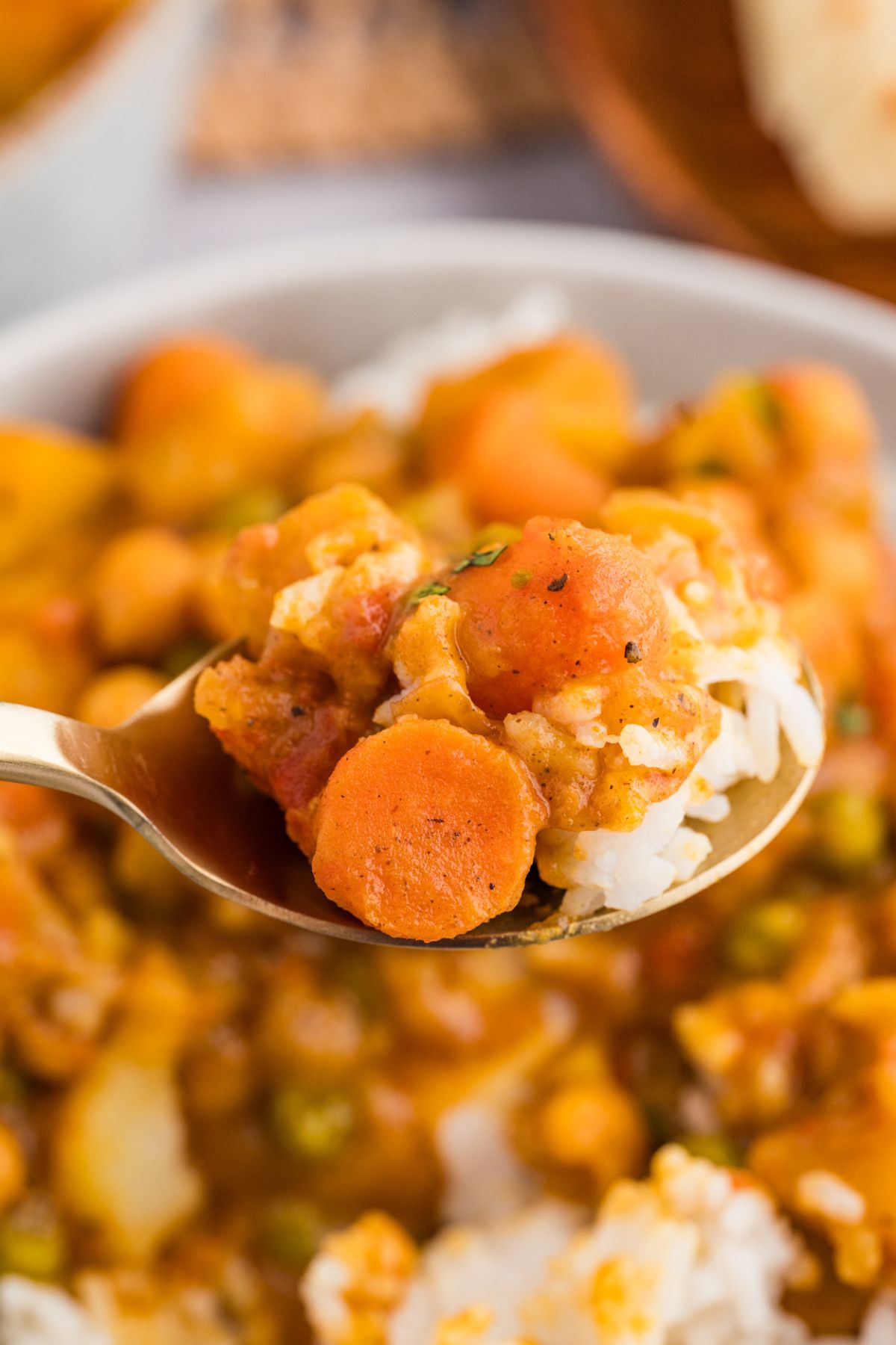 closeup of a silver spoon taking a bite of potato curry with carrots, chickpeas, and steamed white rice.
