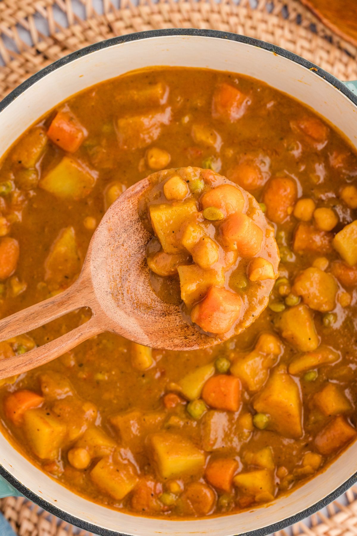 closeup overhead shot of a pot of coconut potato curry with chickpeas with a wooden serving spoon showing the thick sauce texture.