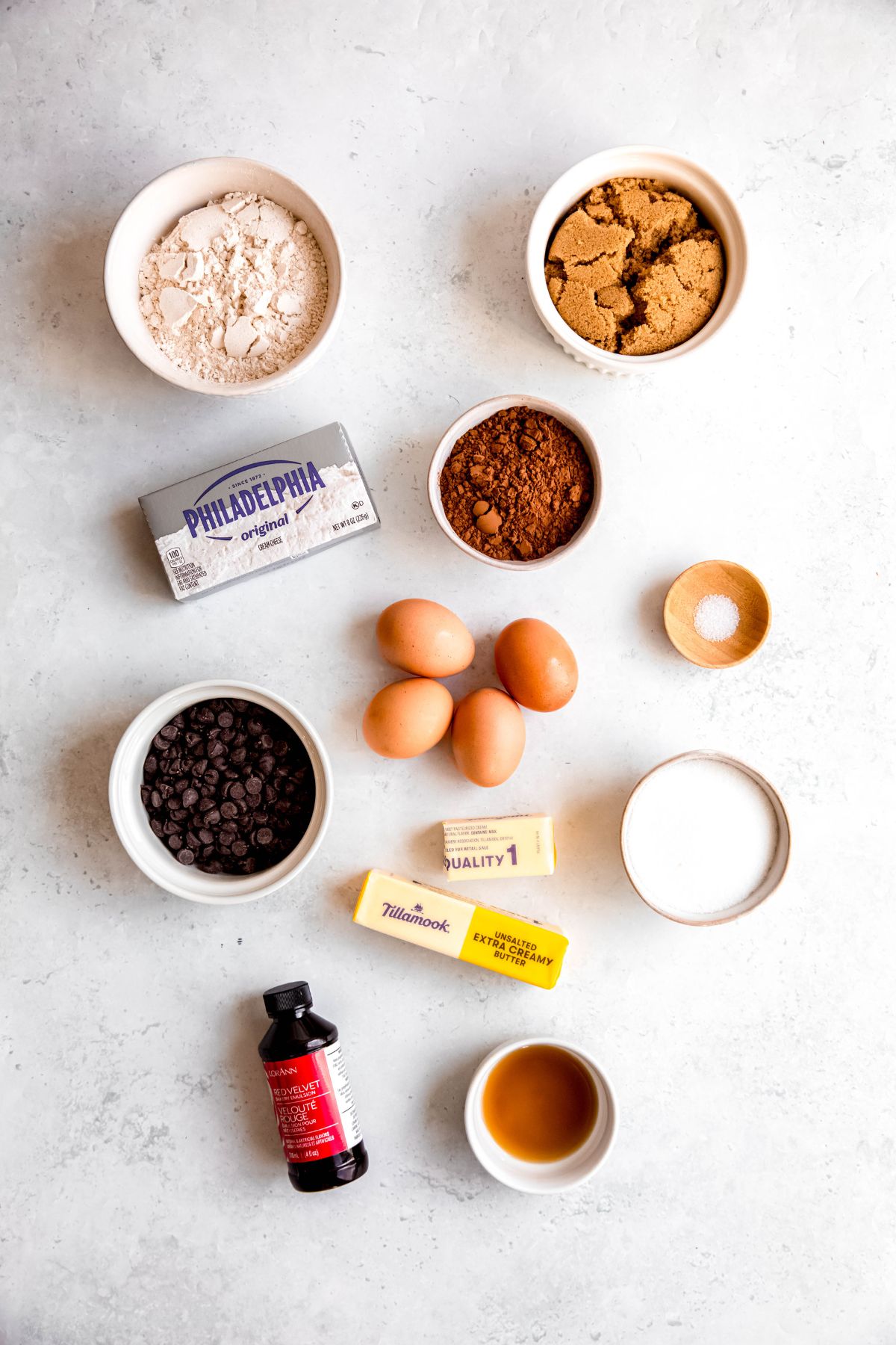 ingredients needed to make red velvet brownies with a cheesecake swirl measured out on a white table.