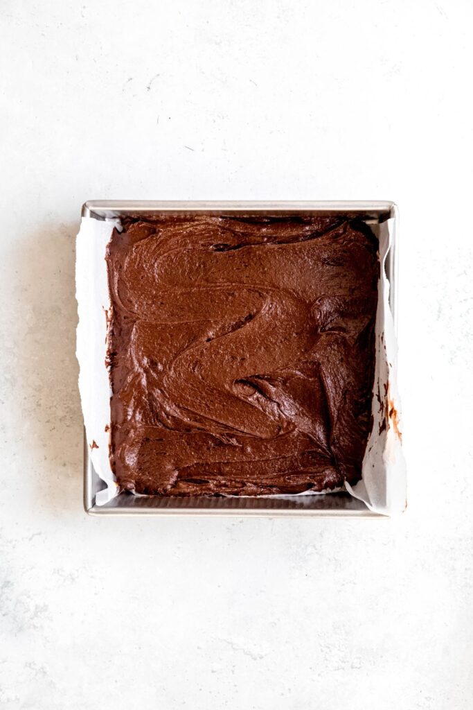 brownie batter spread out in a prepared baking tin.