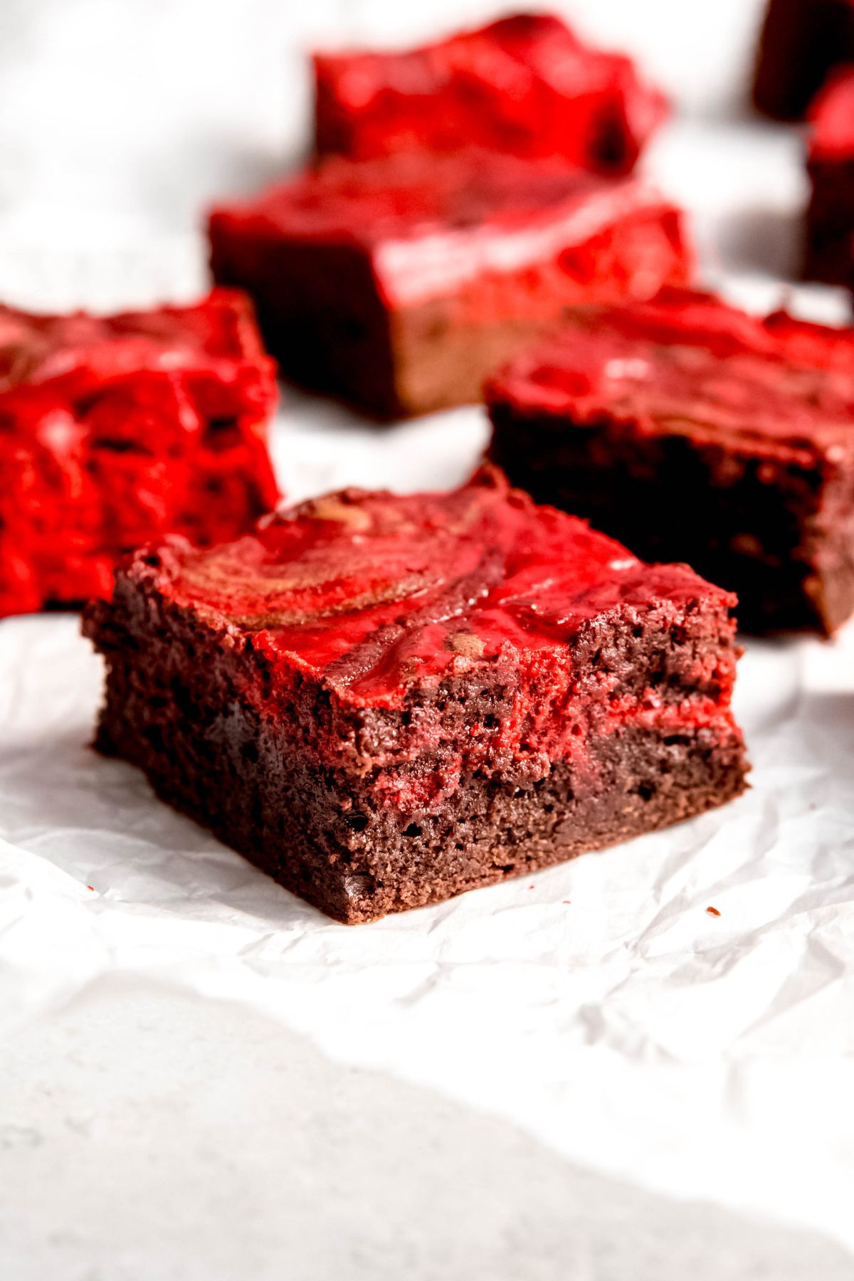 closeup shot of a red velvet brownie from the side showing the chocolate and cheesecake layers swirled together with several more brownies blurred out in the background.