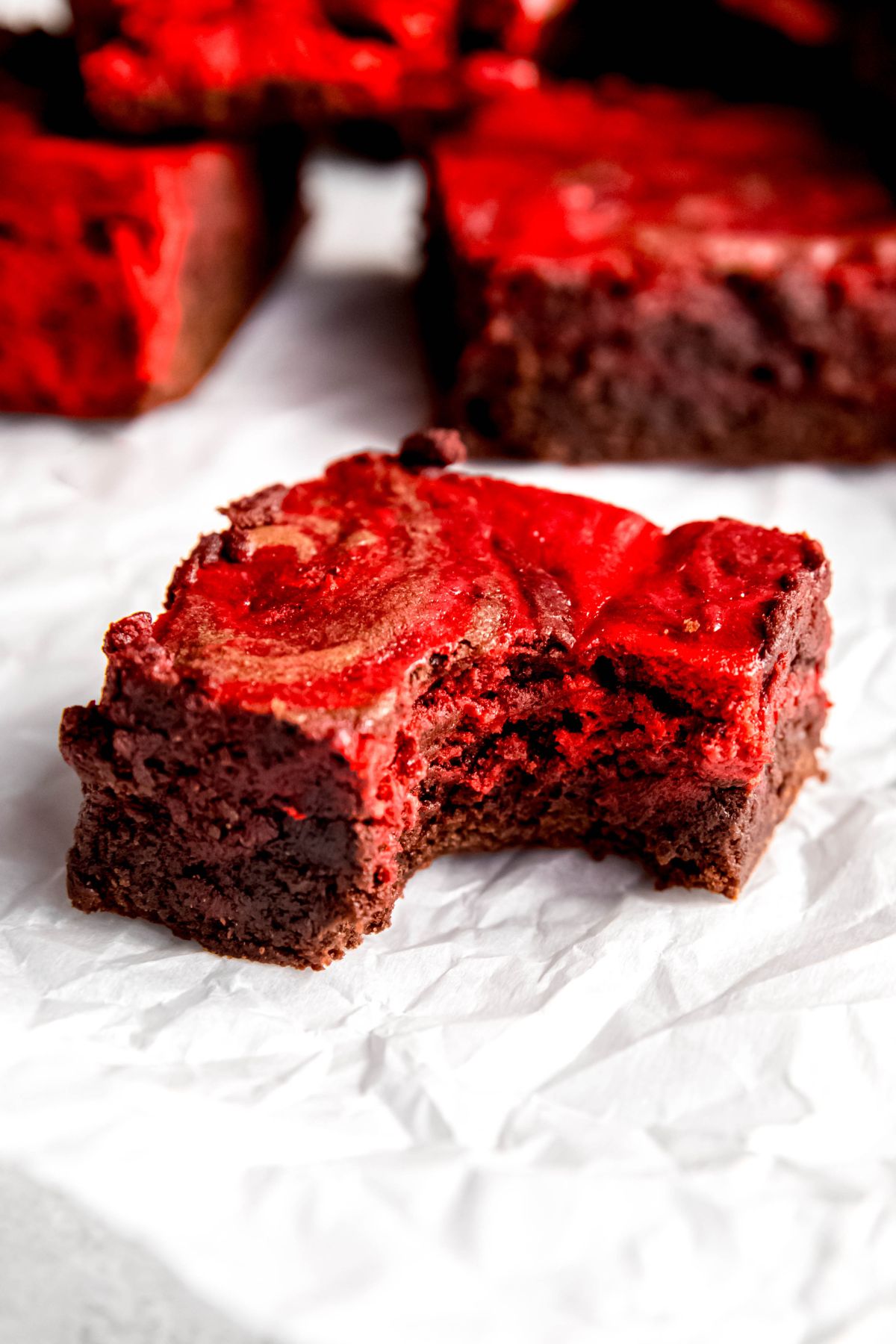 red velvet brownie with a bite taken out showing the fudgy brownie consistency and silky cheesecake swirl.