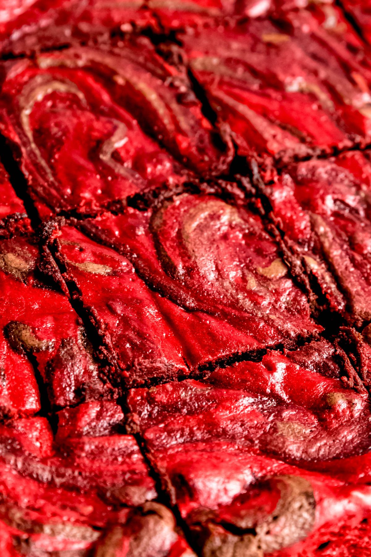 closeup 45 degree angle shot of red velvet cheesecake brownies showing the bright technicolor swirl of the red velvet cheesecake layer with the fudgy brownie base.