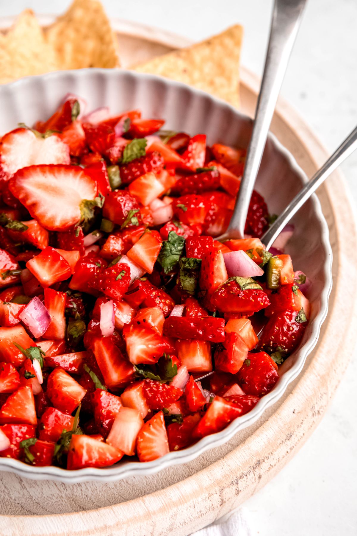 two silver serving spoons in a bowl of fresh strawberry salsa.