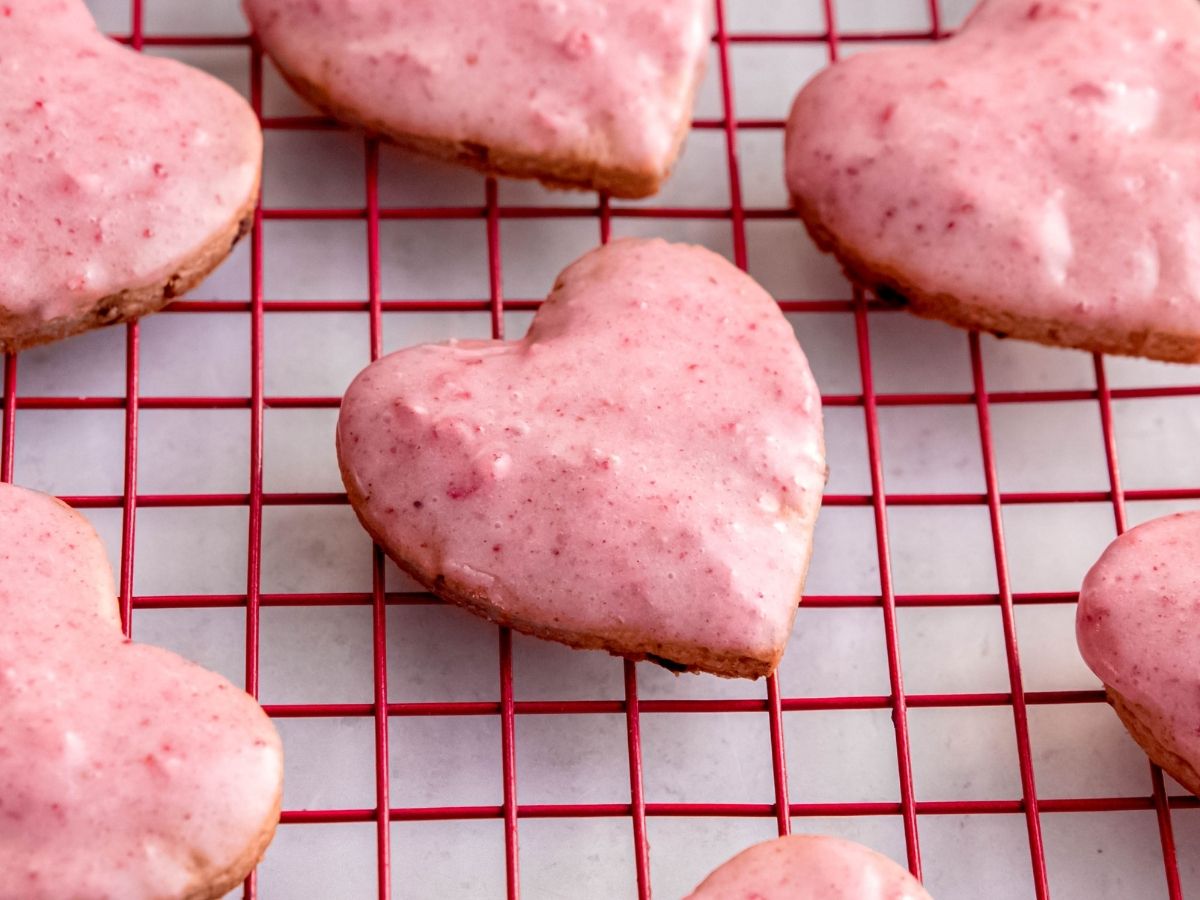 closeup horizontally framed hero shot of strawberry shortbread heart shaped cookies on a red cooling rack.