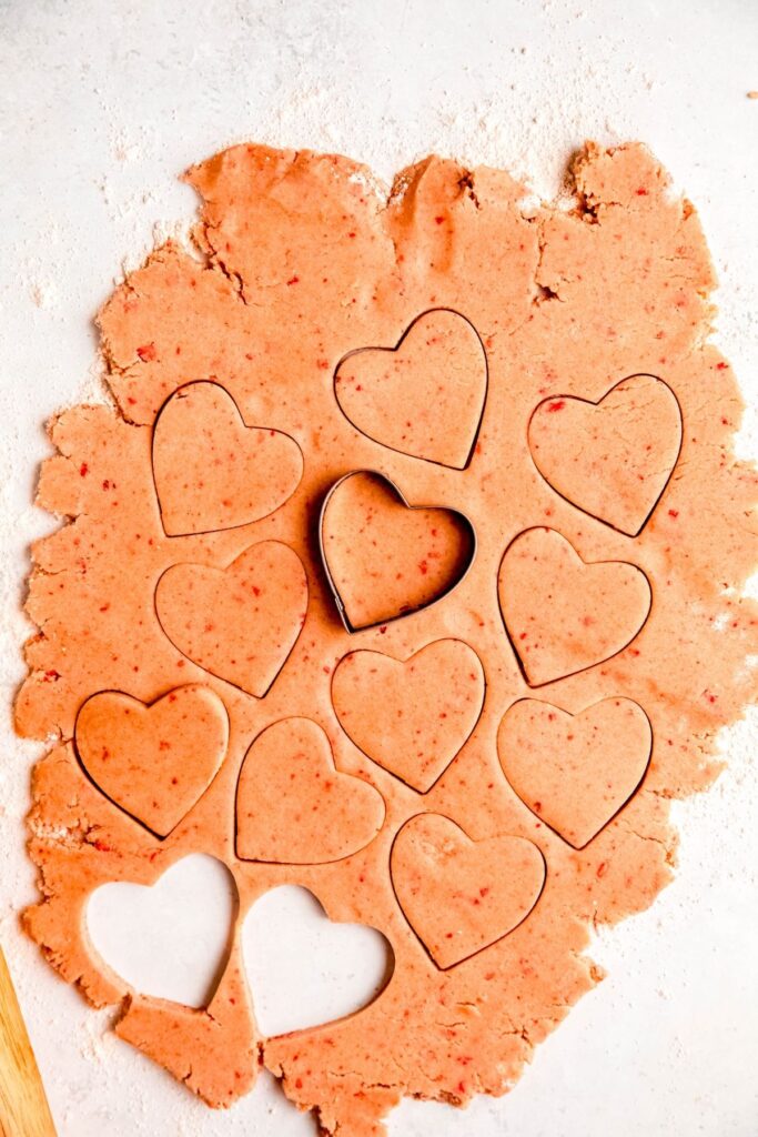 rolled out strawberry shortbread dough being cut into hearts with a cookie cutter.