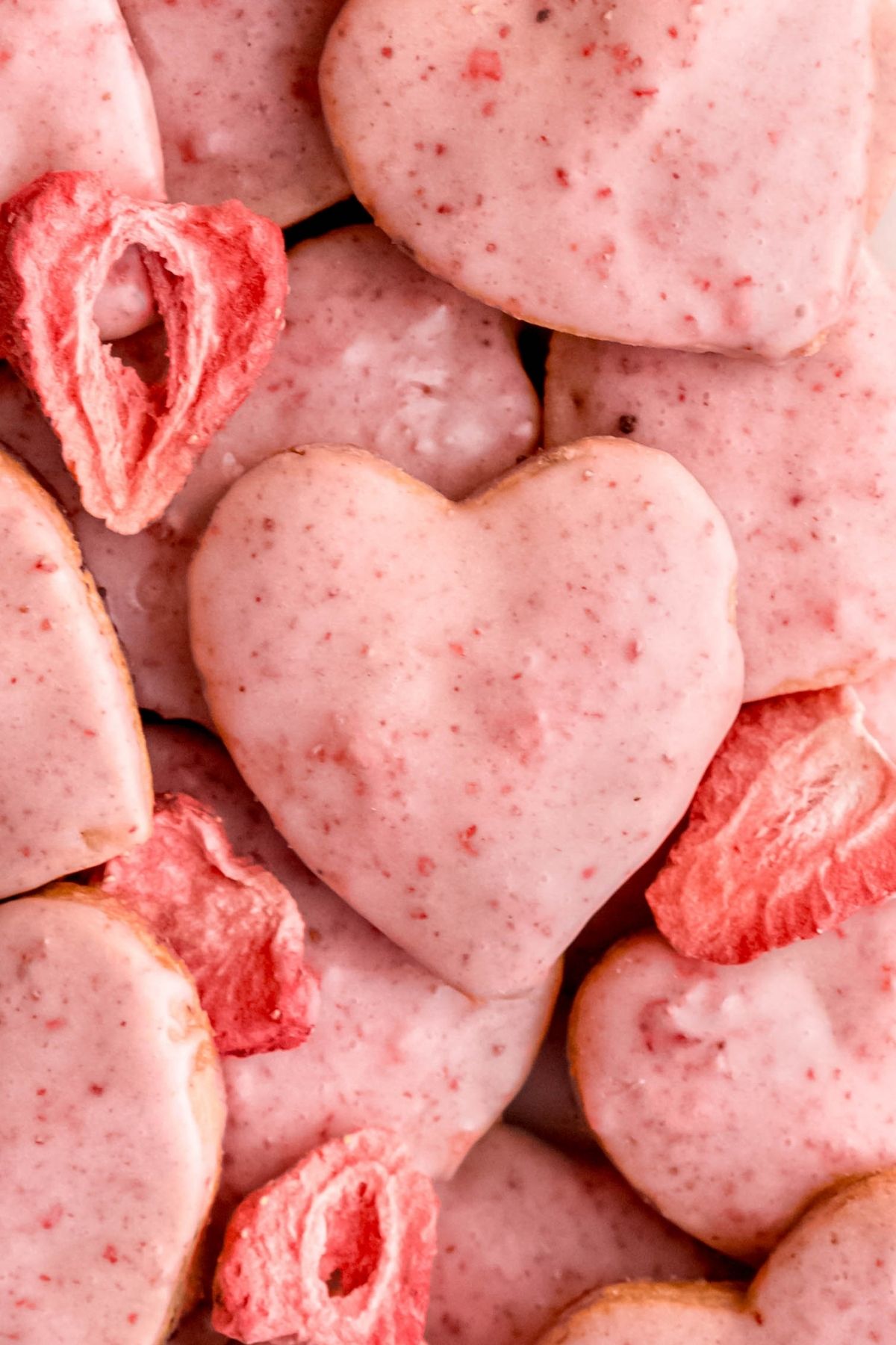 closeup shot of a jumble of heart shaped strawberry shortbread cookies with a few whole freeze dried strawberry halves in the mix.