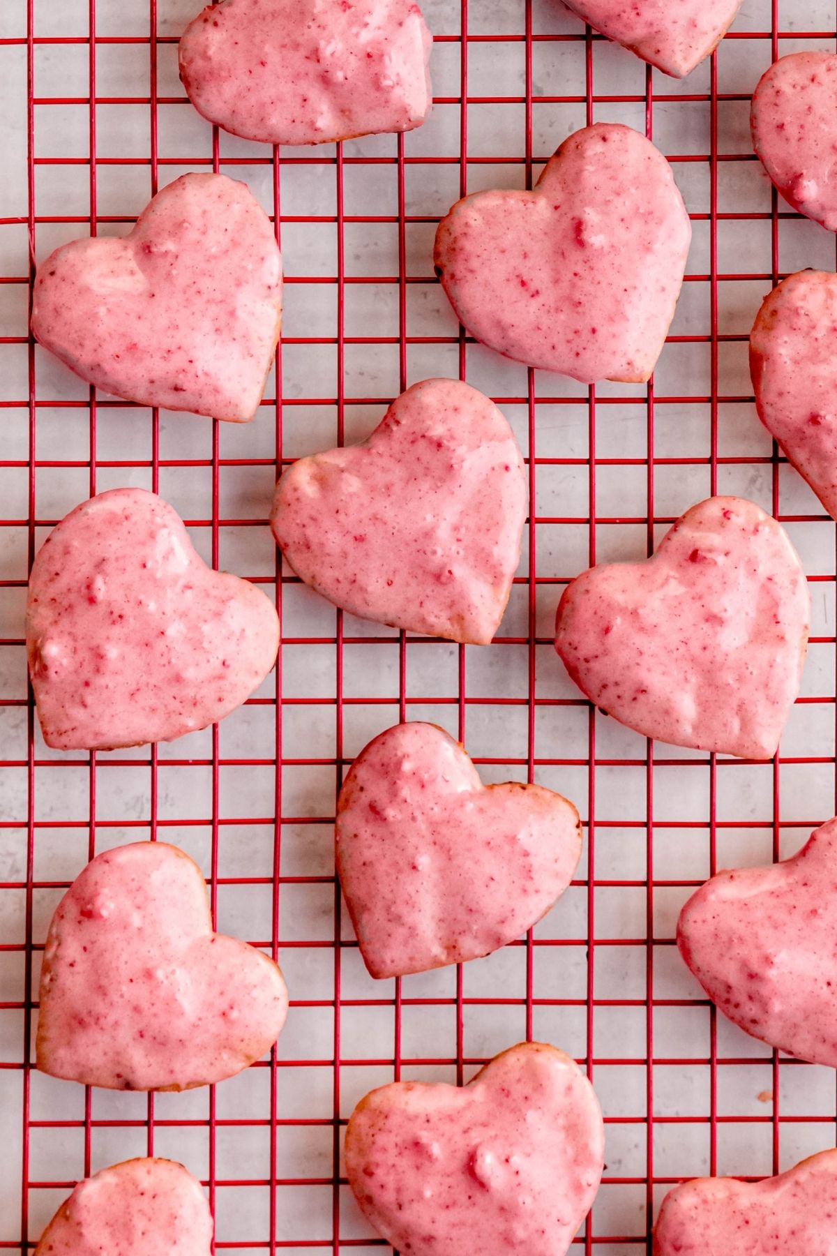 overhead shot of heart shaped strawberry shortbread cookies on a red wire rack above a white table.