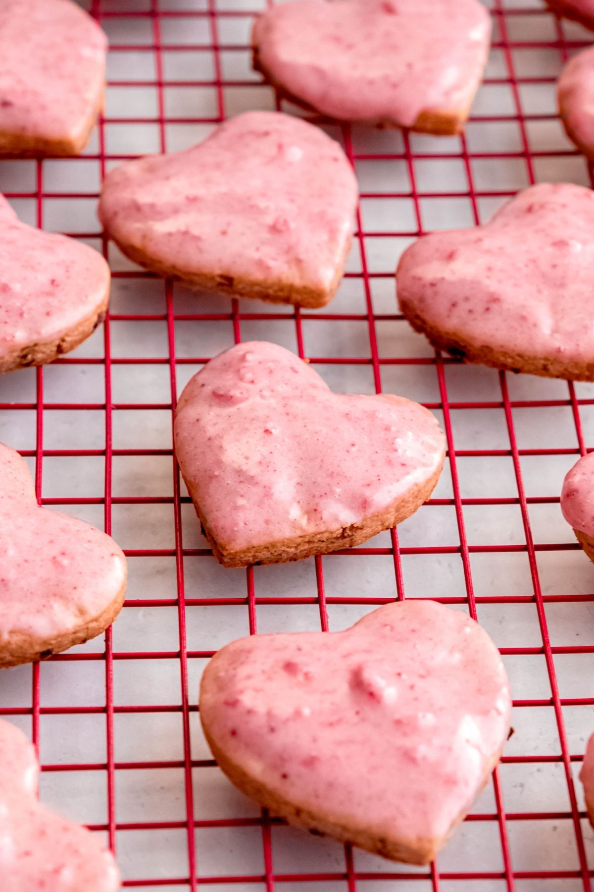 closeup shot of strawberry shortbread cookies in heart shapes on a red cooling rack after dipping in the strawberry milk glaze.