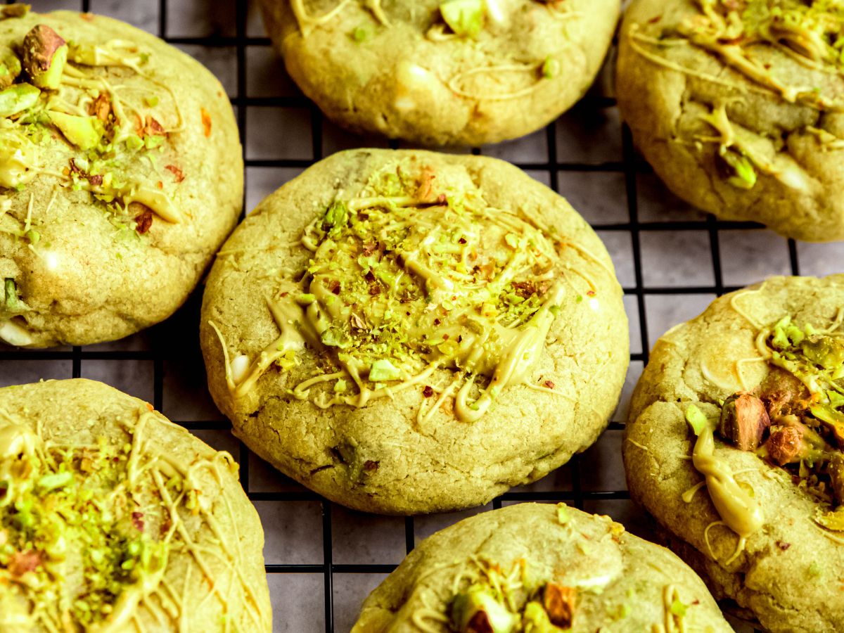 45 degree closeup shot of a black wire rack with pistachio cookies that have been both filled and drizzled with pistachio cream and garnished with chopped pistachios.