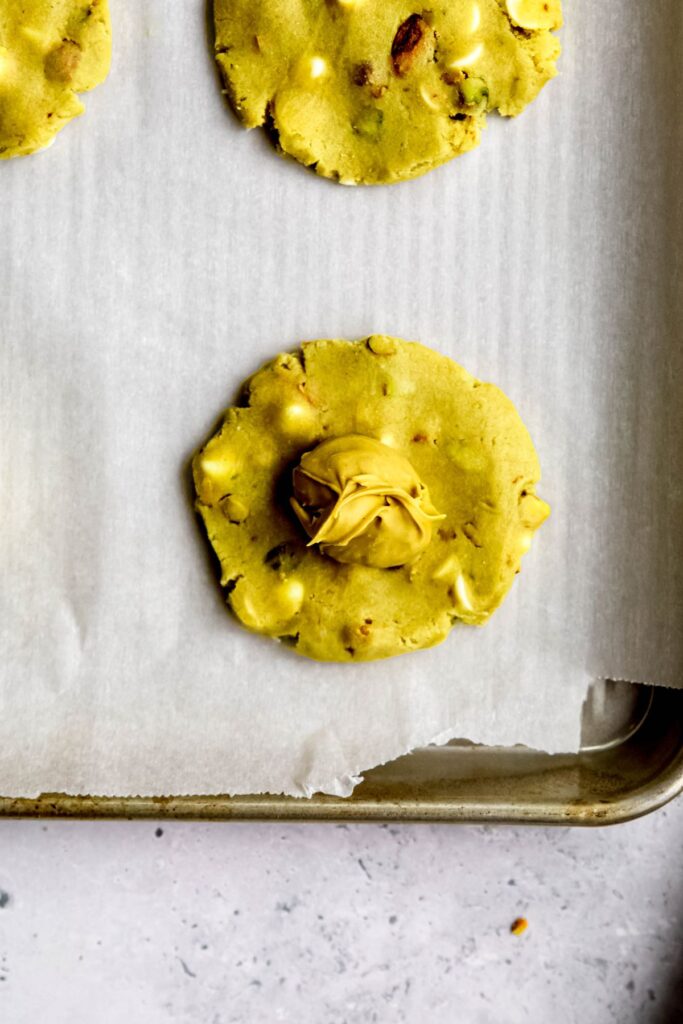 flattened round of raw pistachio cookie dough topped with a frozen dollop of pistachio cream.