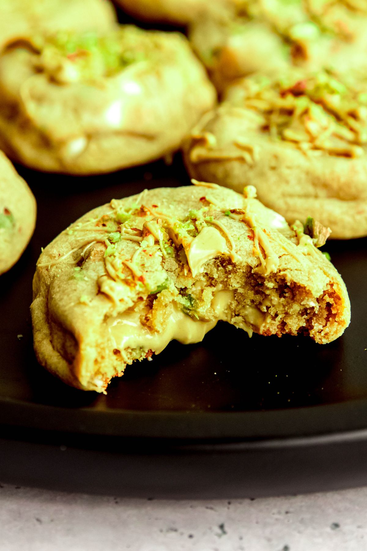 closeup shot of a pistachio cookie on a black plate with a bite taken out showing the creamy pistachio cream filling oozing out a little.