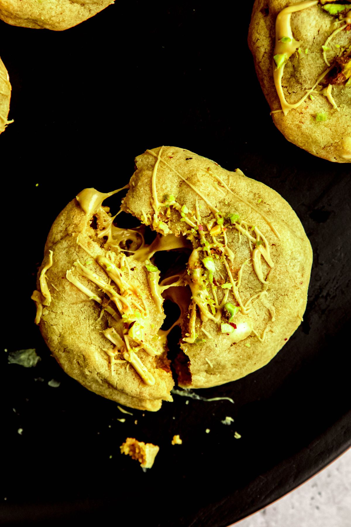 overhead shot of a stuffed pistachio cookie on a black plate, broken in half and slightly pulled apart so the pistachio cream makes threads between the two pieces.