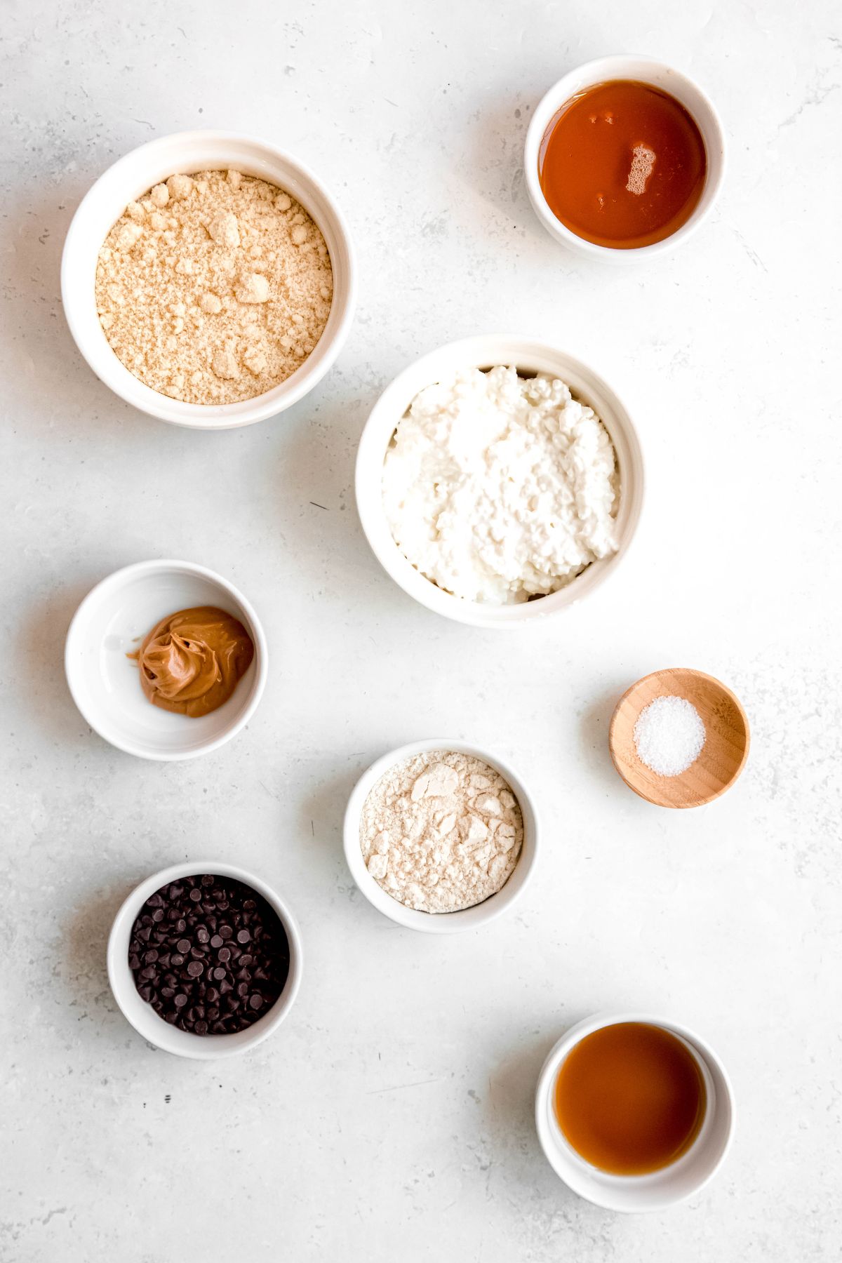 ingredients needed to make viral cottage cheese cookie dough recipe measured out in white bowls on a white table.